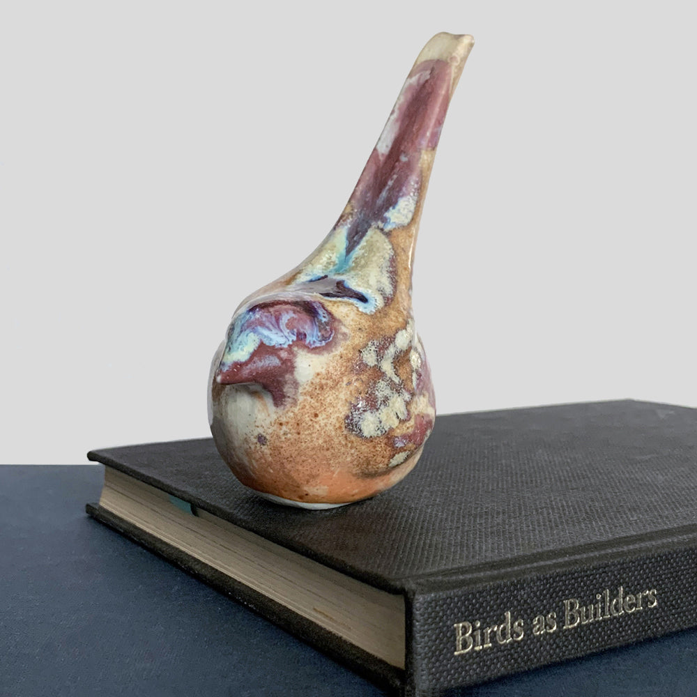 Small ceramic sculpture of a bird, glazed in a rust, cream and blue glaze by artist Becky Story.