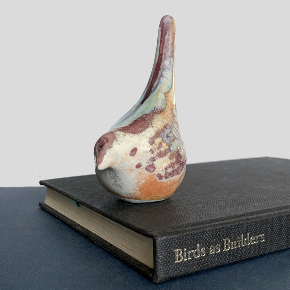 Small ceramic sculpture of a bird, glazed in a rust, cream and blue glaze by artist Becky Story.
