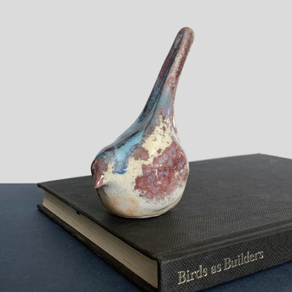 Small ceramic sculpture of a bird, glazed in a rust, cream and blue glaze by artist Becky Story.