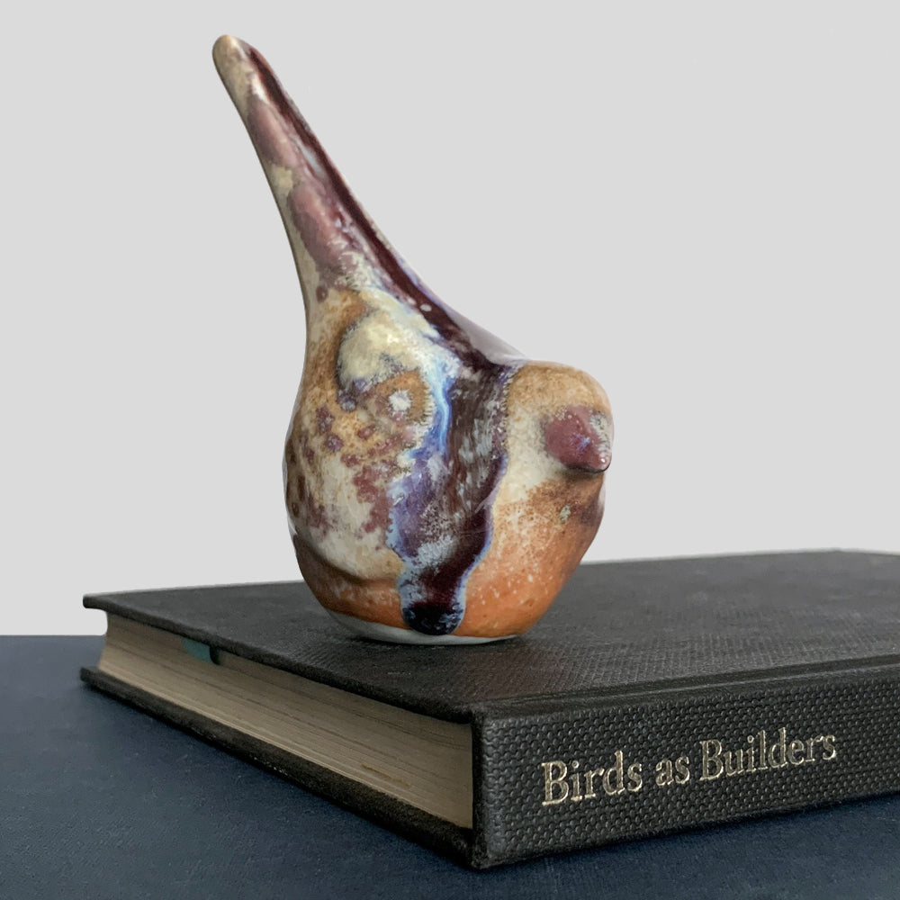 Small ceramic sculpture of a bird, glazed in a rust, cream and blue glaze by artist Becky Story.