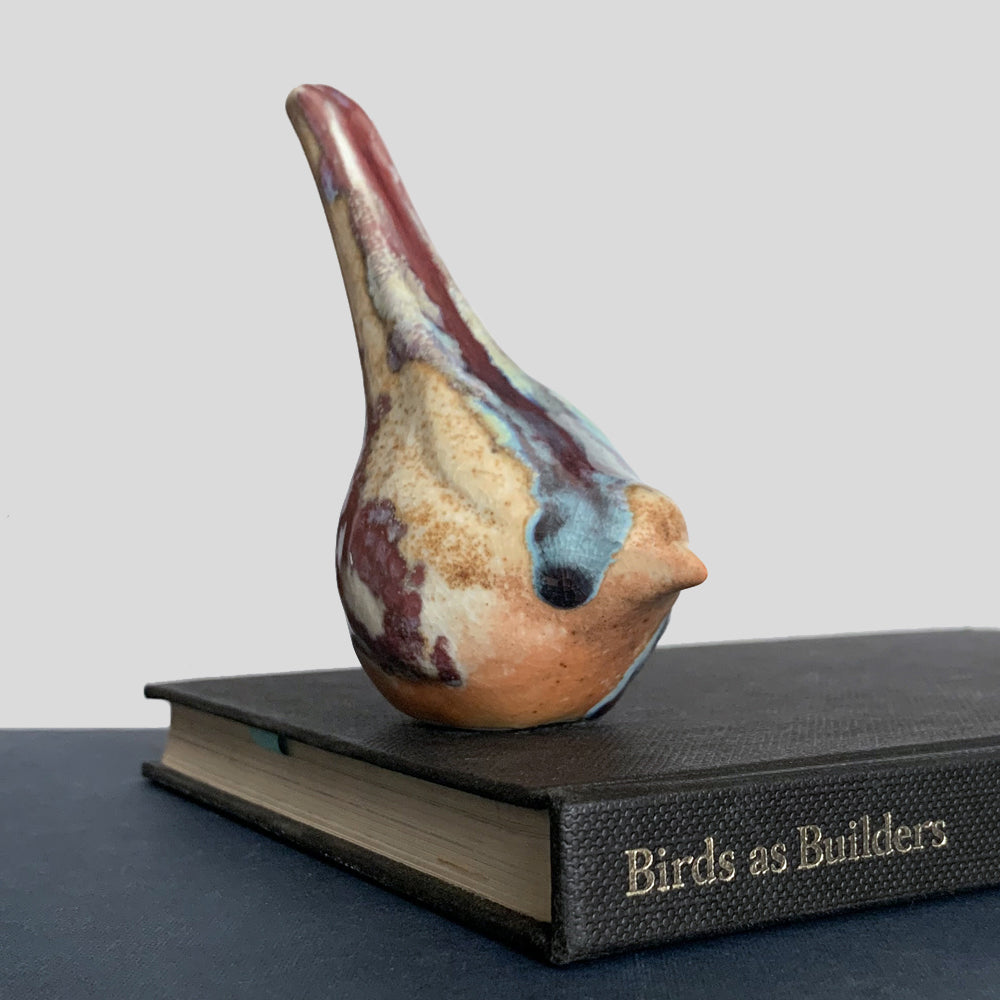Small ceramic sculpture of a bird, glazed in a rust, cream and blue glaze by artist Becky Story.