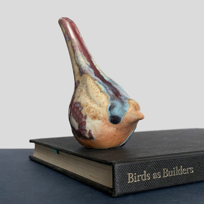 Small ceramic sculpture of a bird, glazed in a rust, cream and blue glaze by artist Becky Story.