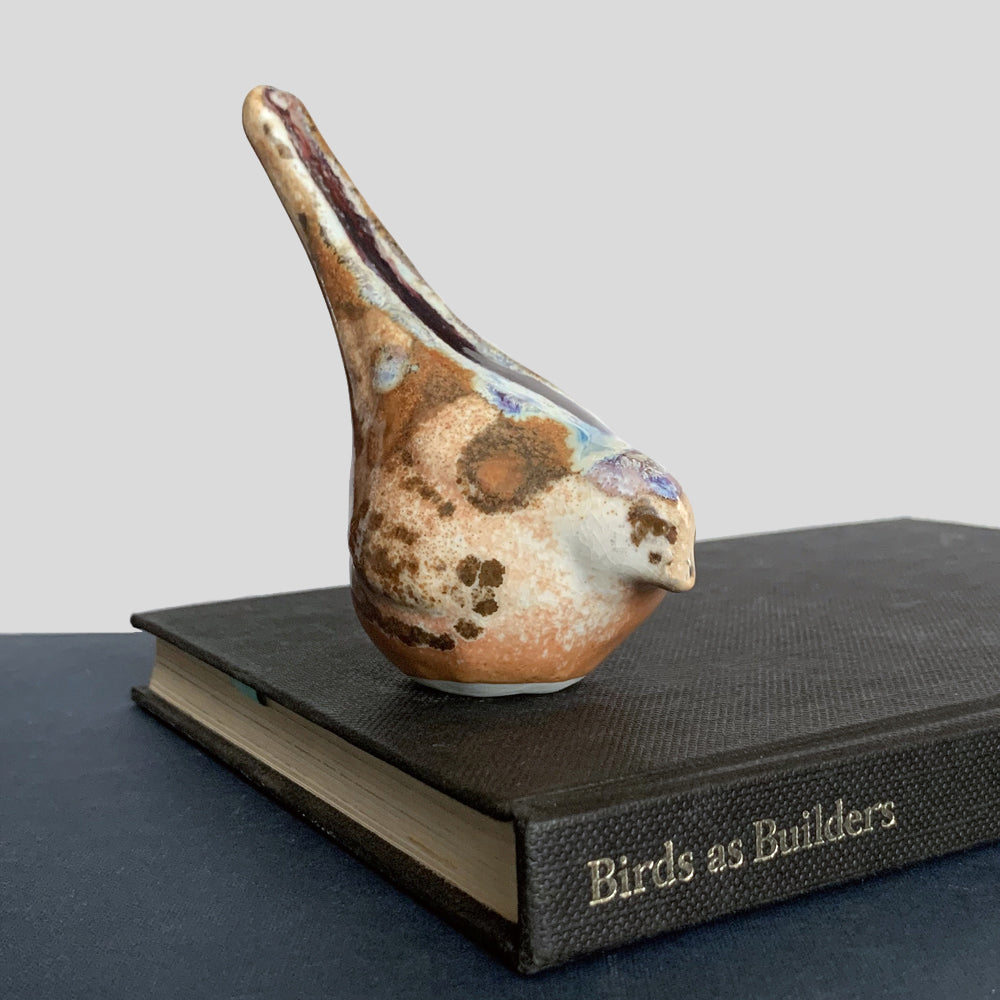 Small ceramic sculpture of a bird, glazed in a rust, cream and blue glaze by artist Becky Story.