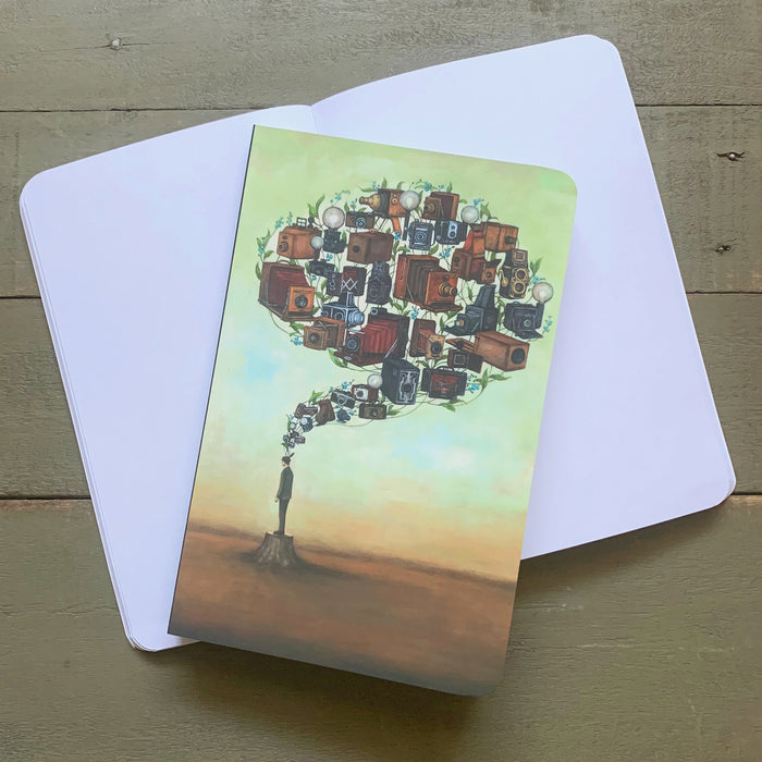 Duy Huynh notebook featuring his "Photographic Memory Brainstem" artwork, a man standing on a tree stump with vintage cameras and forget-me-not flowers rising above into the shape of a brain. Blank notebook pages.