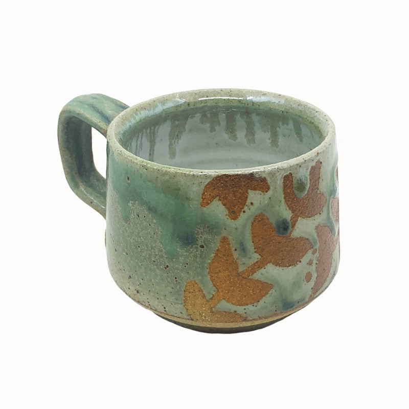 Heather Ossandon handmade, woodfired mug, angled view. Light green with rusty botanical pattern.