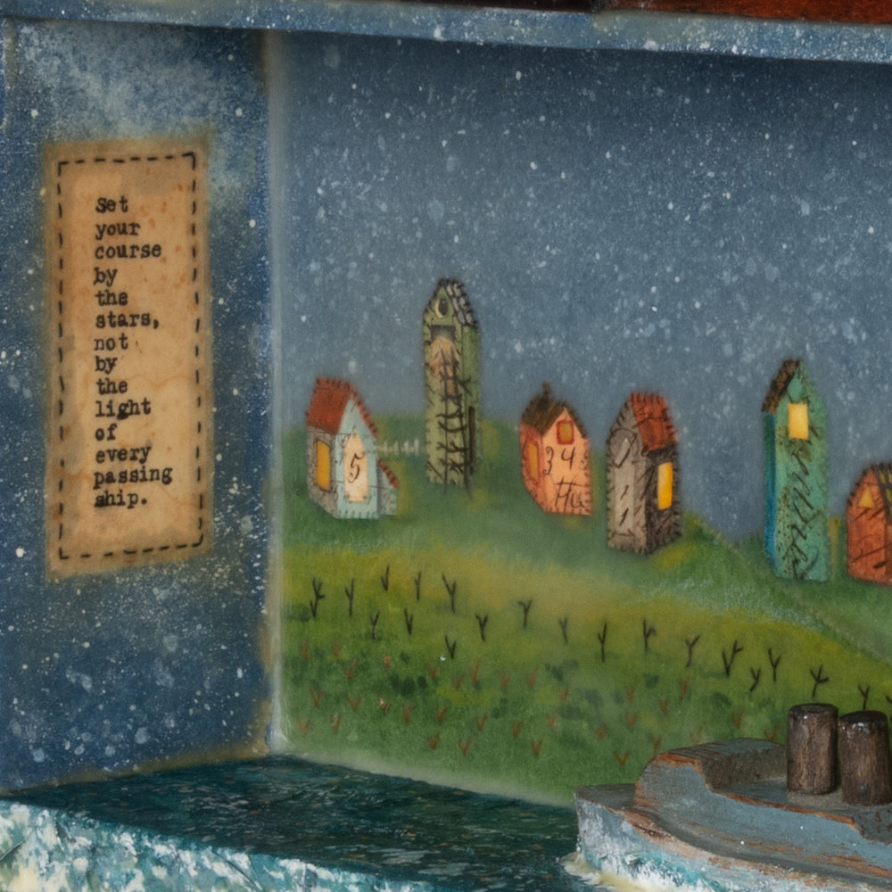 Detail of "By the Stars" mixed media encaustic assemblage by Janet Eskridge.  A wooden box with top finial, Janet's artwork fills the interior - a row of houses under a star filled sky, with a wooden boat in the water.