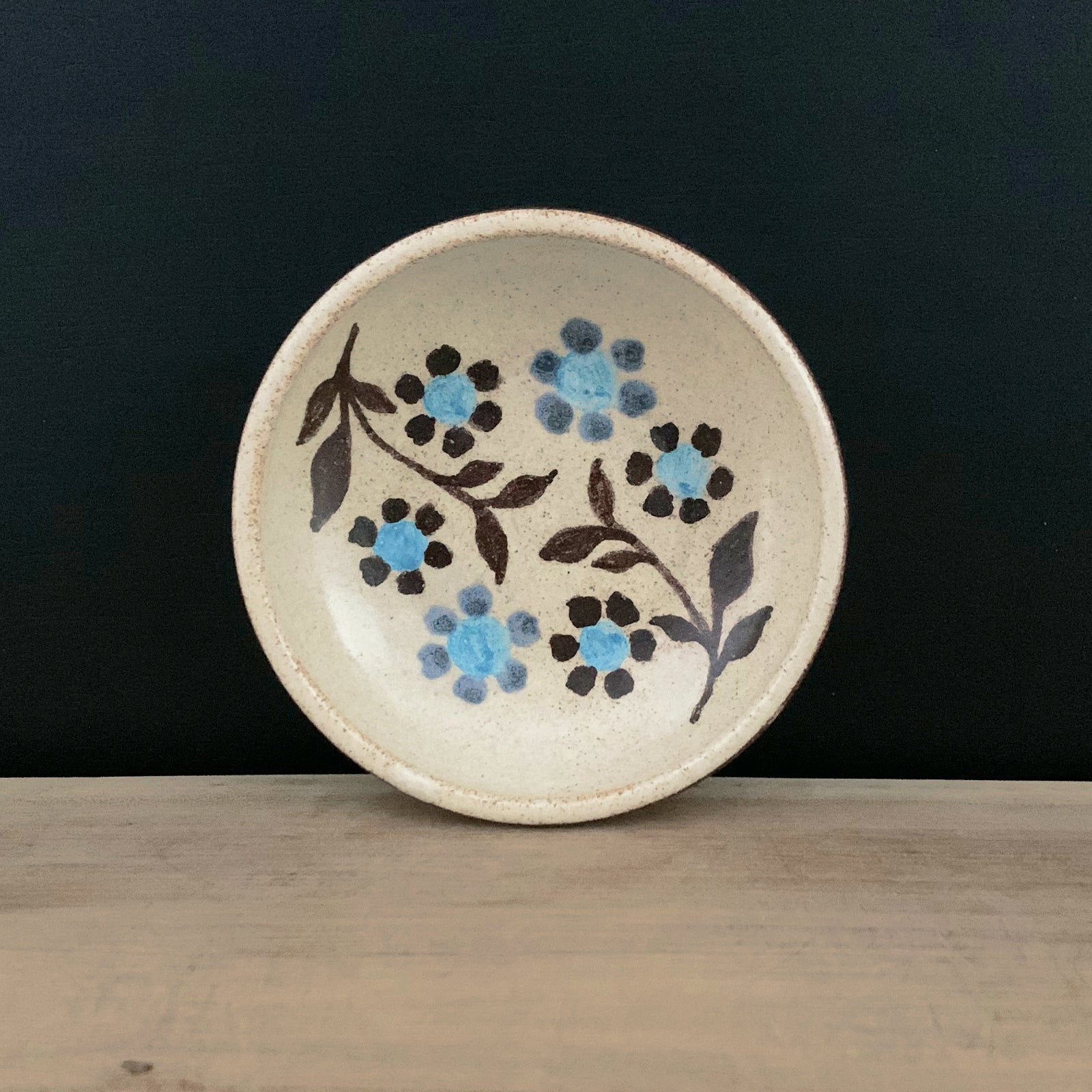 Handmade pottery from Off Menu Pots. Small round catchall dish with blue flowers, handmade. Shown with black background.