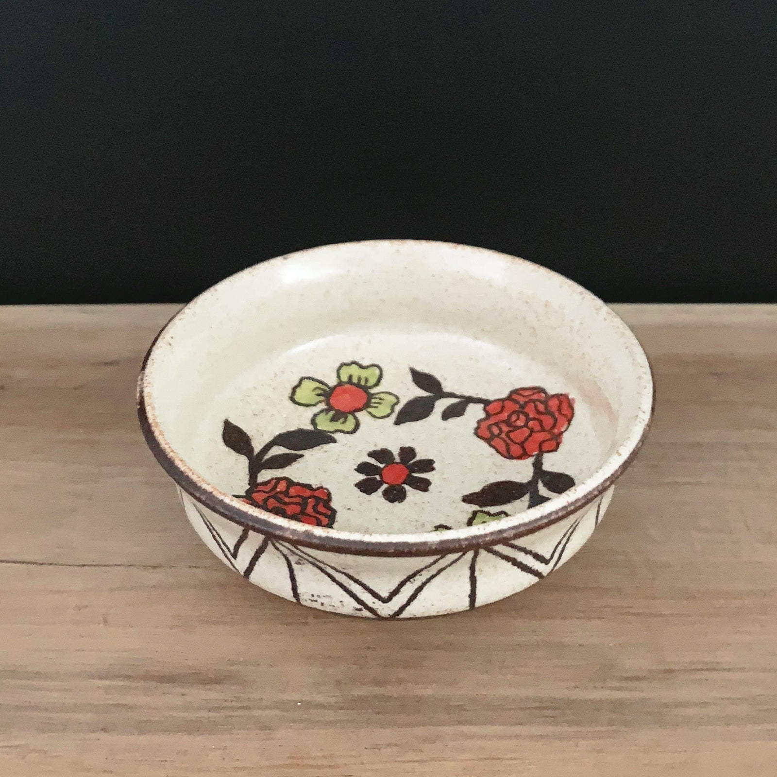 Handmade pottery from Off Menu Pots. Small round catchall dish with red and chartreuse flowers, handmade. Side view.