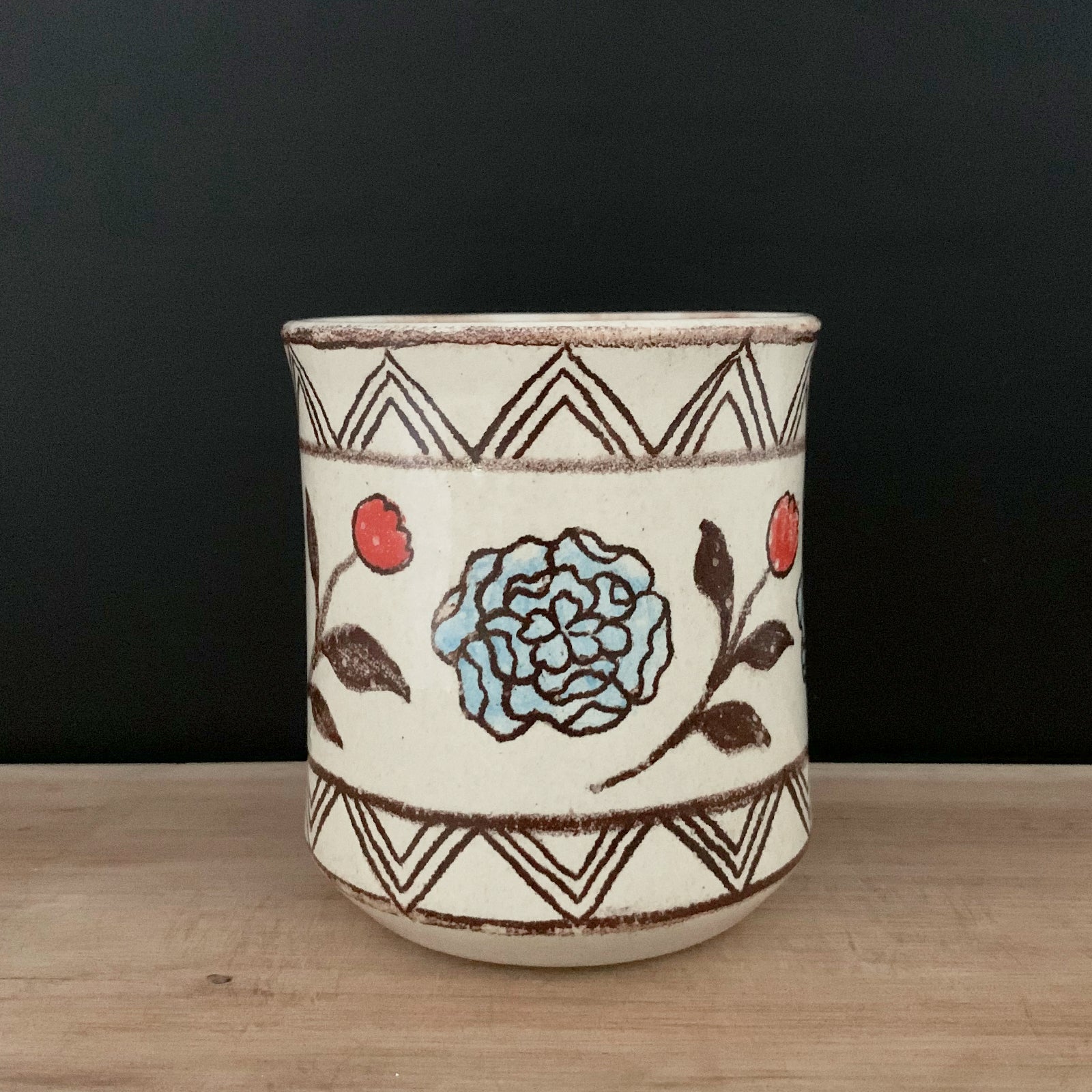 Handmade pottery from Off Menu Pots. Cup with blue and red flowers. Shown on black background.