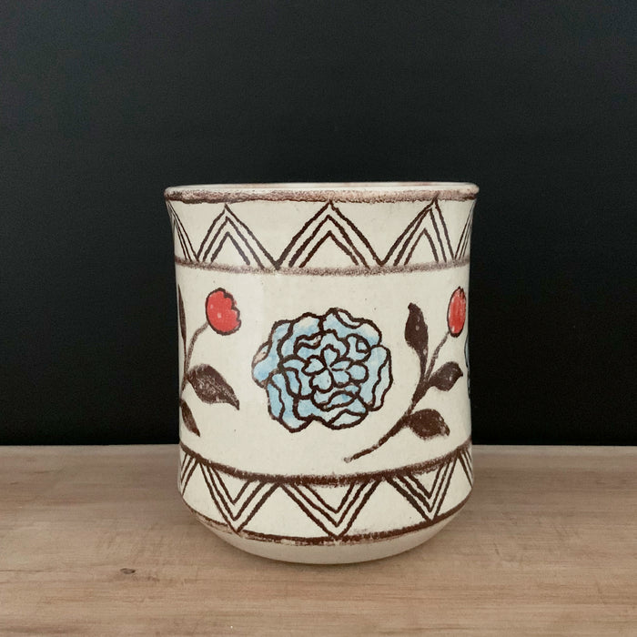 Handmade pottery from Off Menu Pots. Cup with blue and red flowers. Shown on black background.