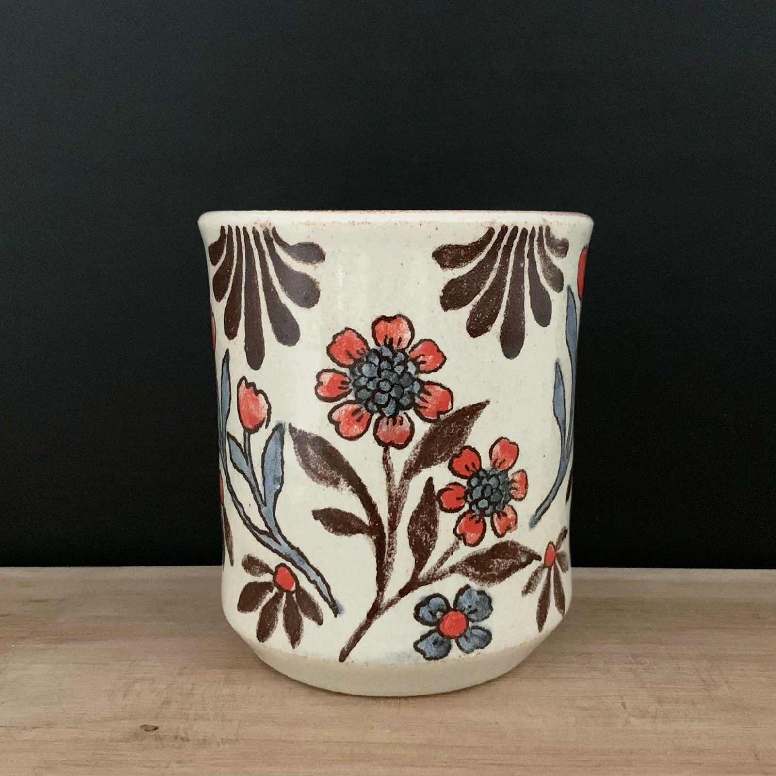 Handmade pottery from Off Menu Pots. Cup with red flowers. Shown with black background.