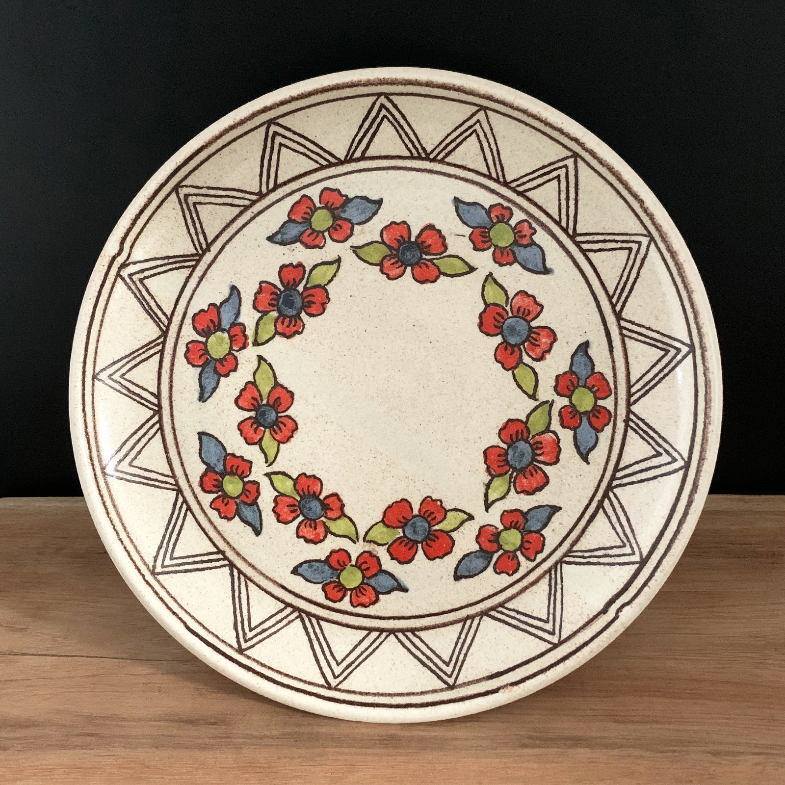 Handmade pottery from Off Menu Pots. Dessert plate with blue, red and chartreuse flowers. Shown on black background.