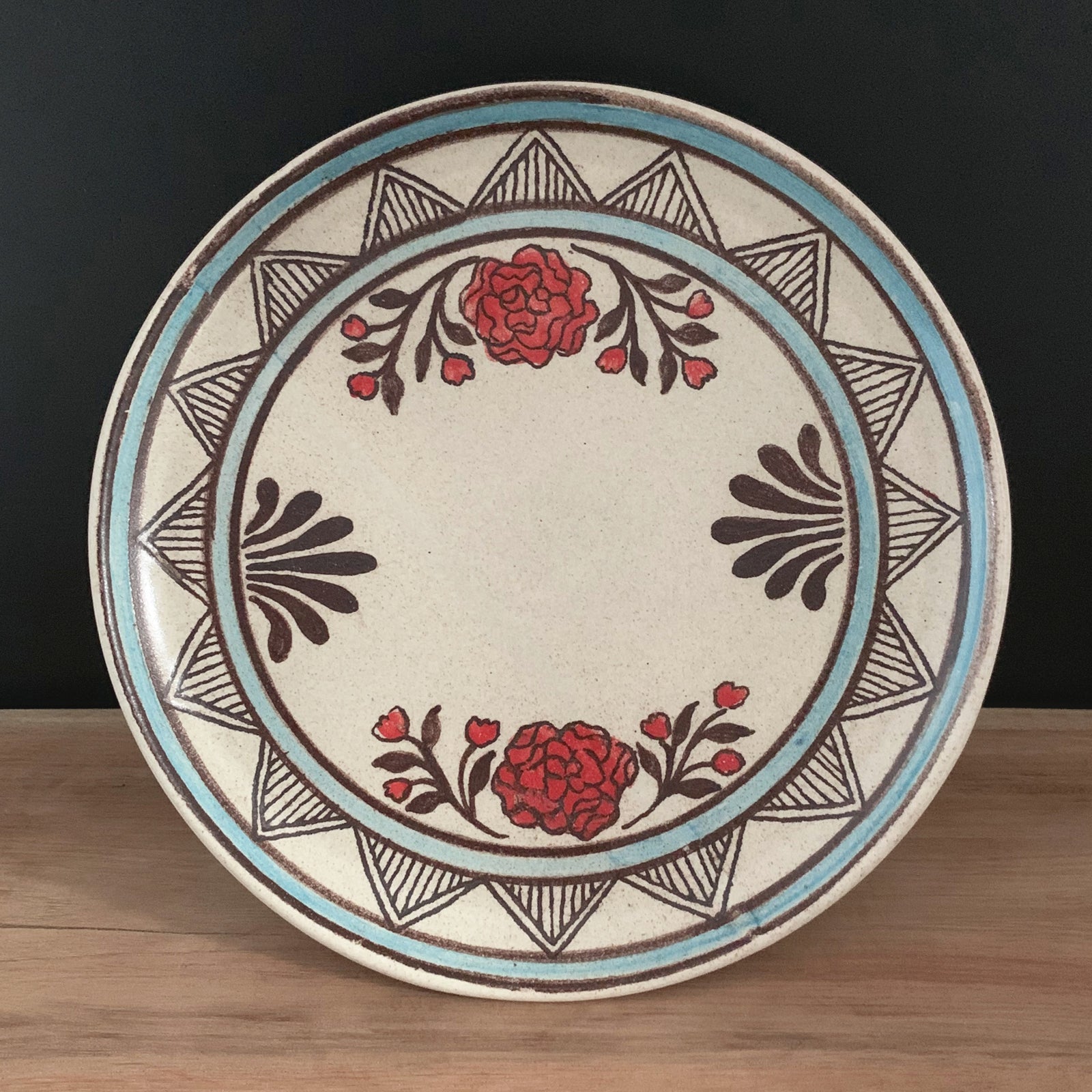 Handmade pottery from Off Menu Pots. Dessert plate with red flowers. Shown with black background.