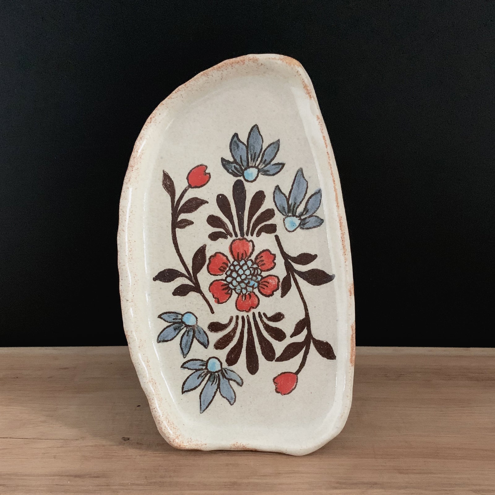 Handmade pottery from Off Menu Pots. Small dish with blue and red flowers on black background.