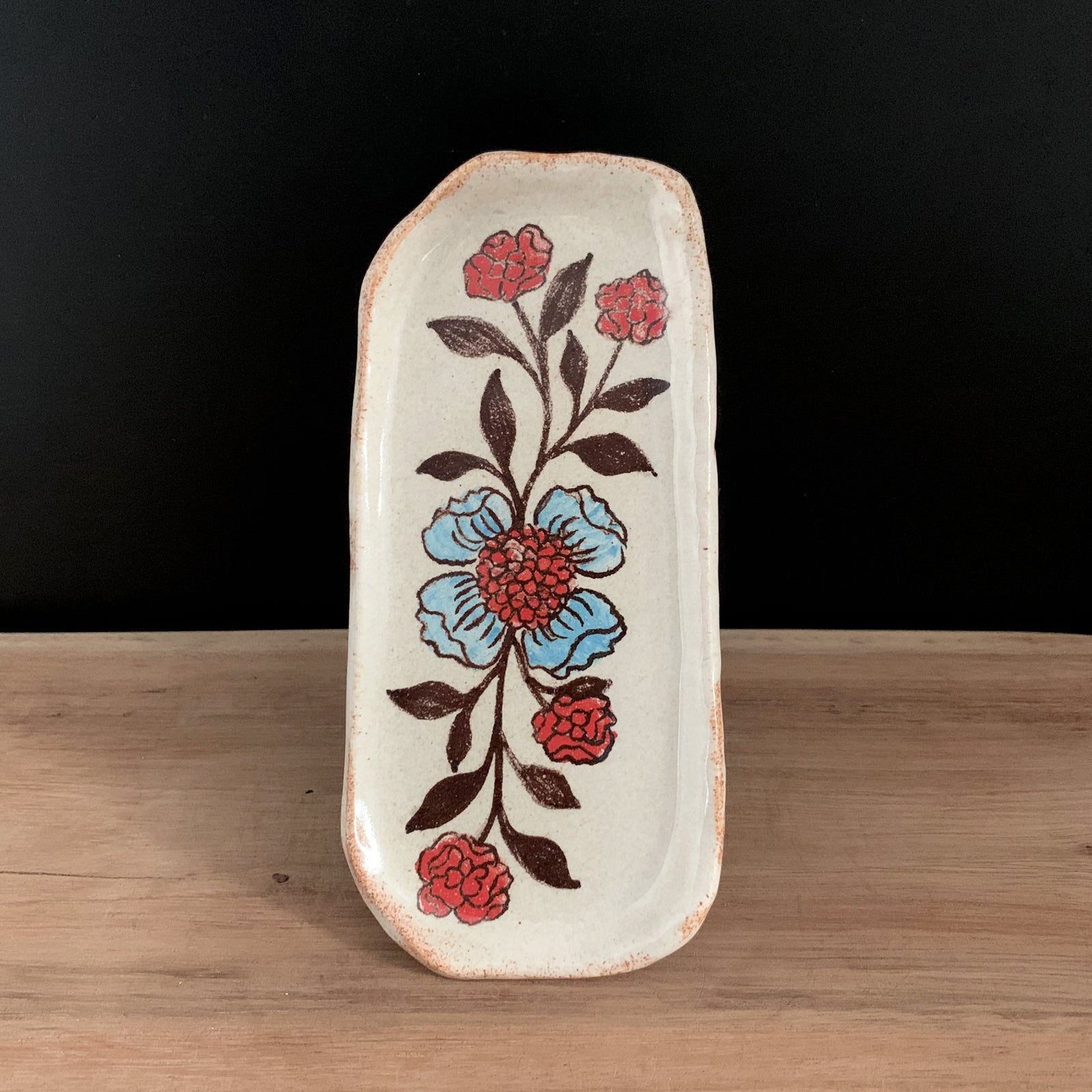 Handmade pottery from Off Menu Pots. Small dish with blue and red flowers on black background.
