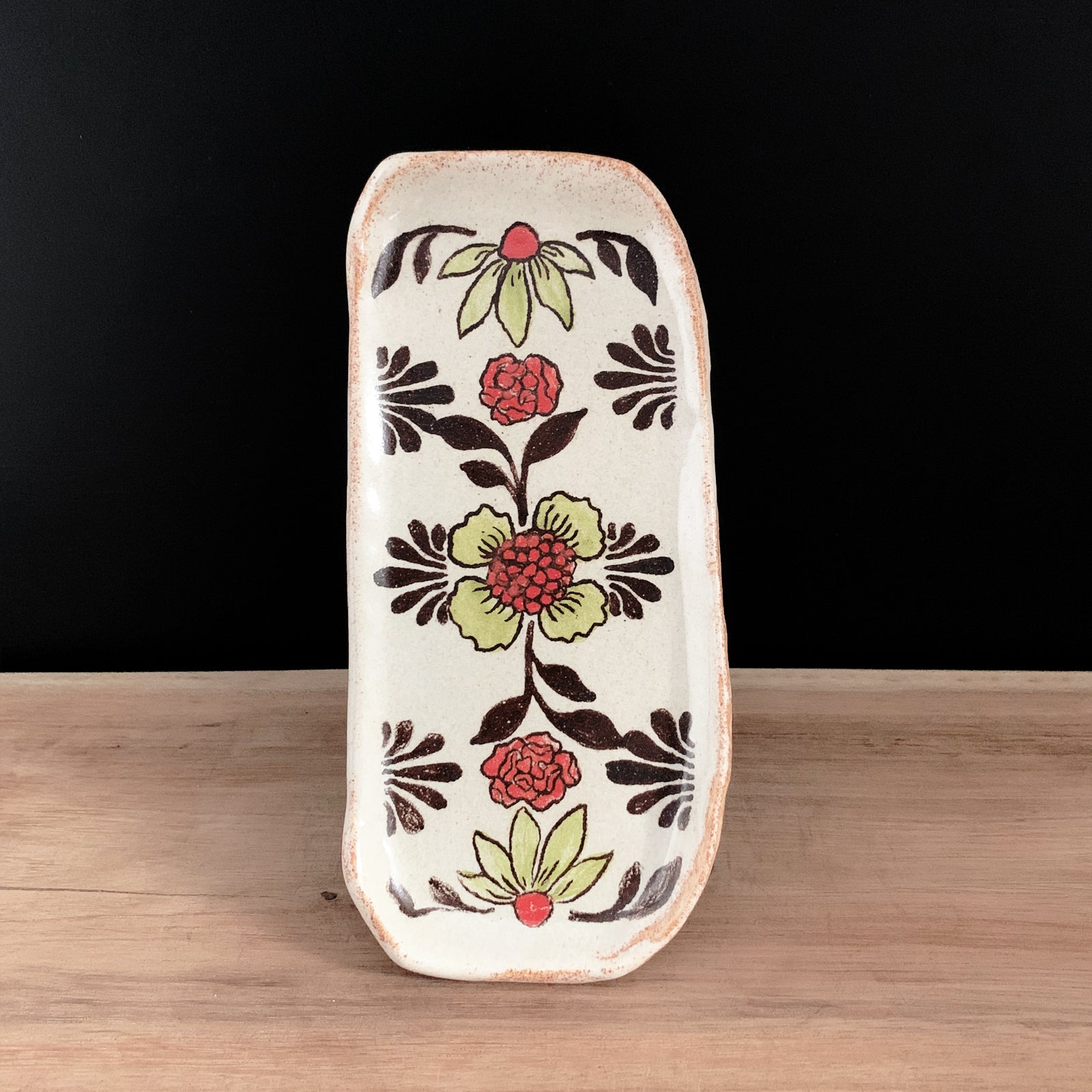Handmade pottery from Off Menu Pots. Small dish with red and chartreuse flowers on black background.