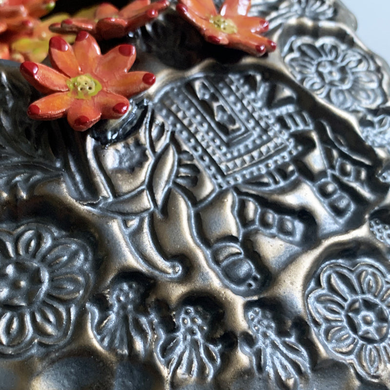 Handmade ceramic wall niche by Paula Smith. Clay face is stamped with flower patterns and an elephant, finished in a gunmetal glaze. There are three dimensional  orange flowers. Elephant detail shown.