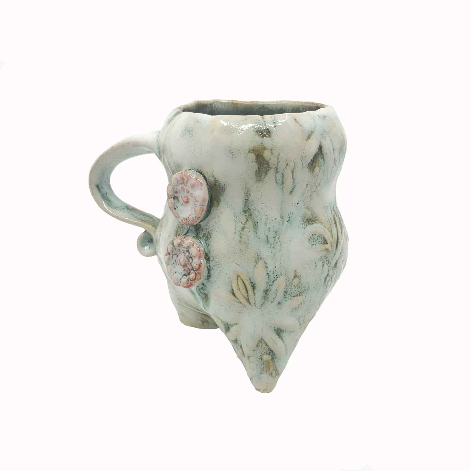 Handmade ceramic cup by artist Paula Smith. Curvy cup with handle, creamy white  body with floral detail, decorated with pink buttons. Side angle view.