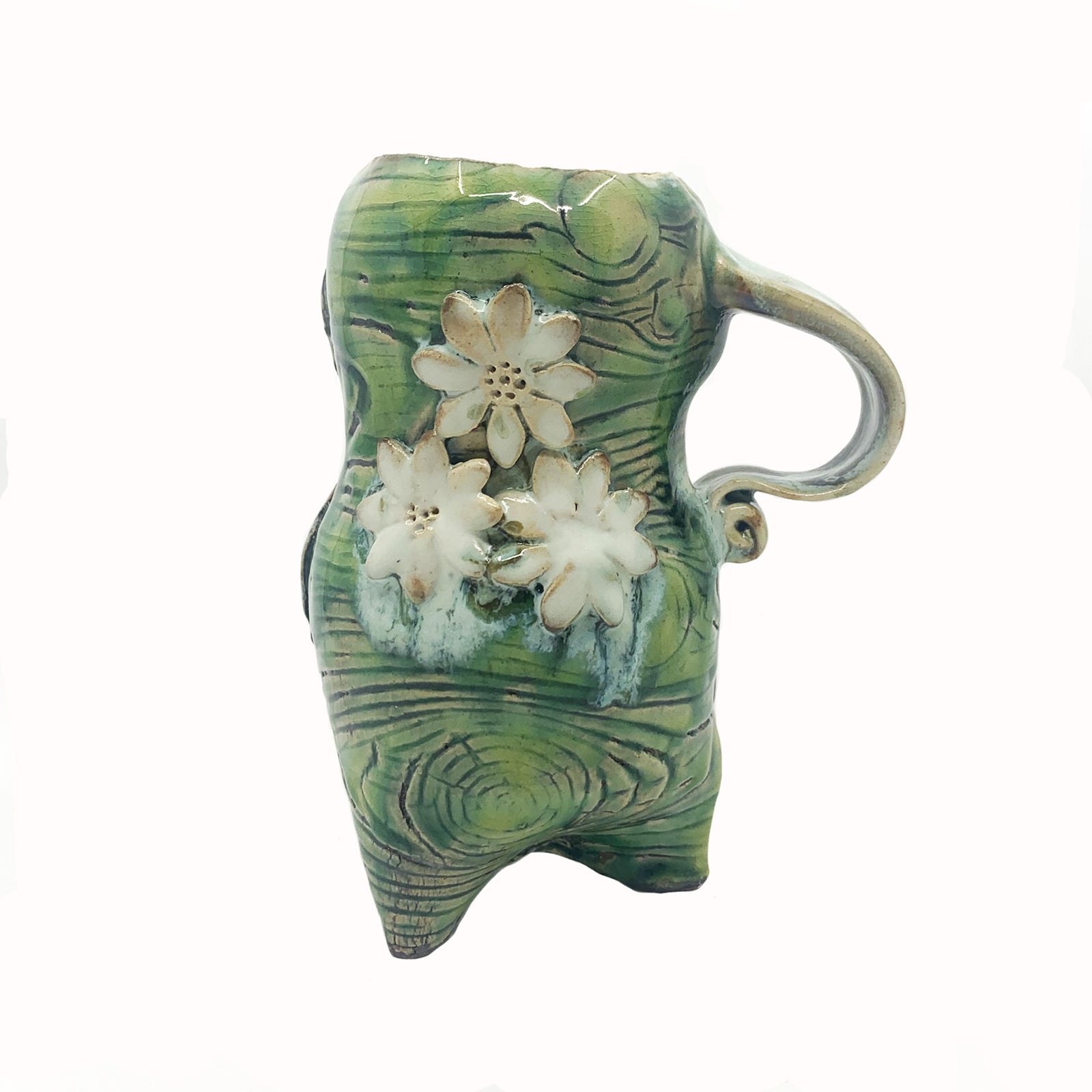 Handmade ceramic cup by artist Paula Smith. Curvy cup with handle, green body with woodgrain detail, decorated with white flowers and white fig leaf on reverse side.