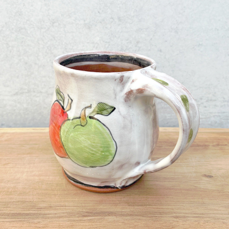 Handmade ceramic mug by NC potter Molly Lithgo. White with red and green apple decoration. View with handle detail.
