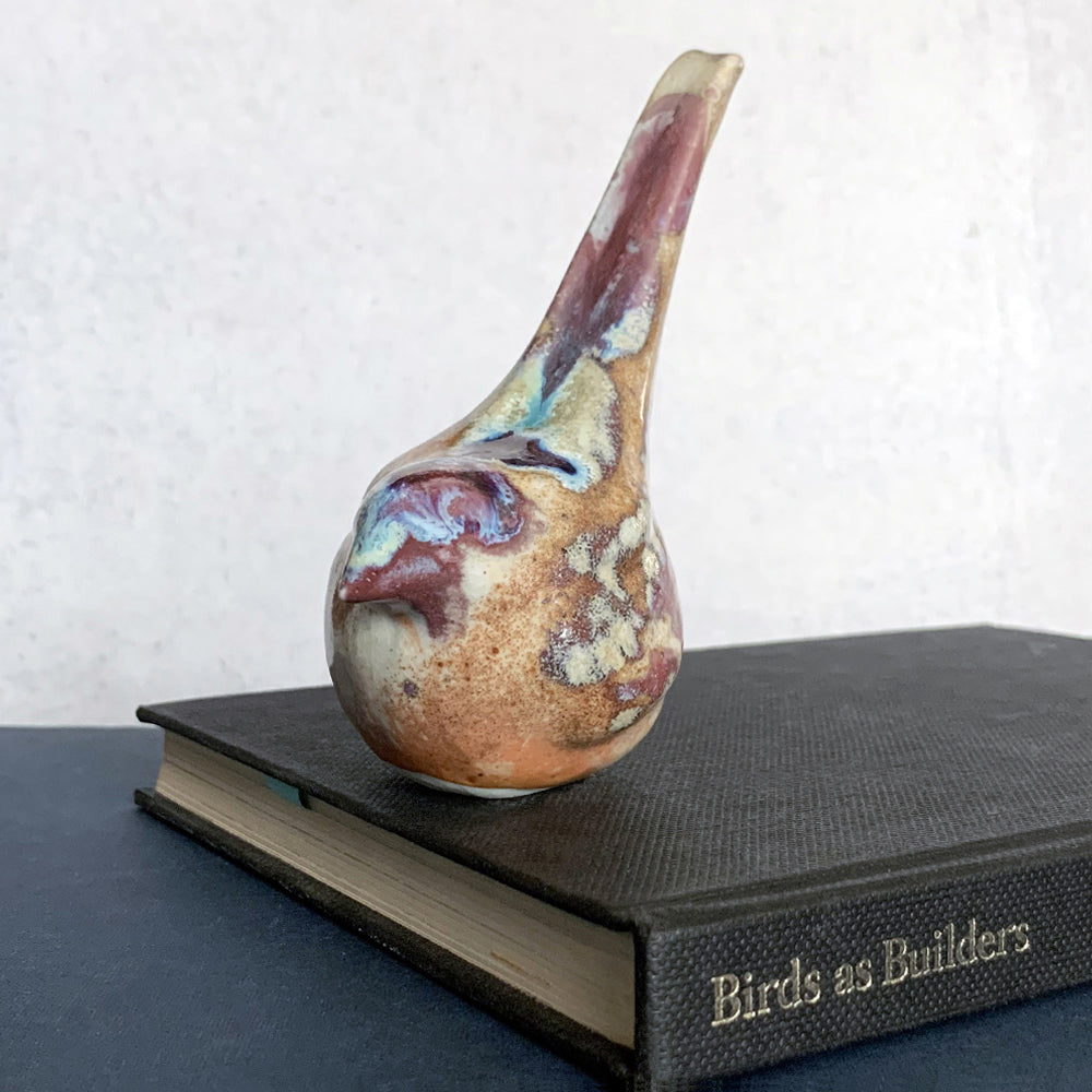Small ceramic sculpture of a bird, glazed in a rust, cream and blue glaze by artist Becky Story. 