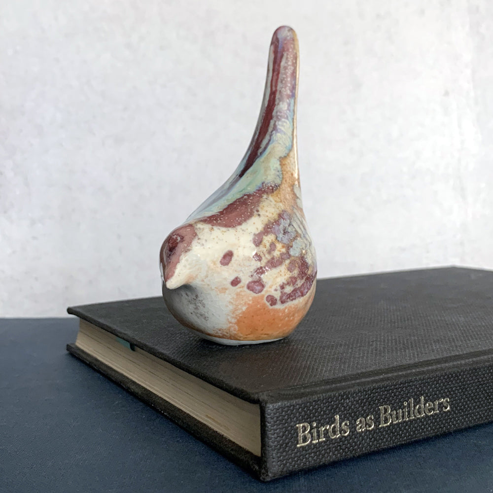 Small ceramic sculpture of a bird, glazed in a rust, cream and blue glaze by artist Becky Story. 