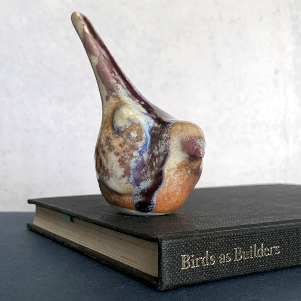 Small ceramic sculpture of a bird, glazed in a rust, cream and blue glaze by artist Becky Story. 