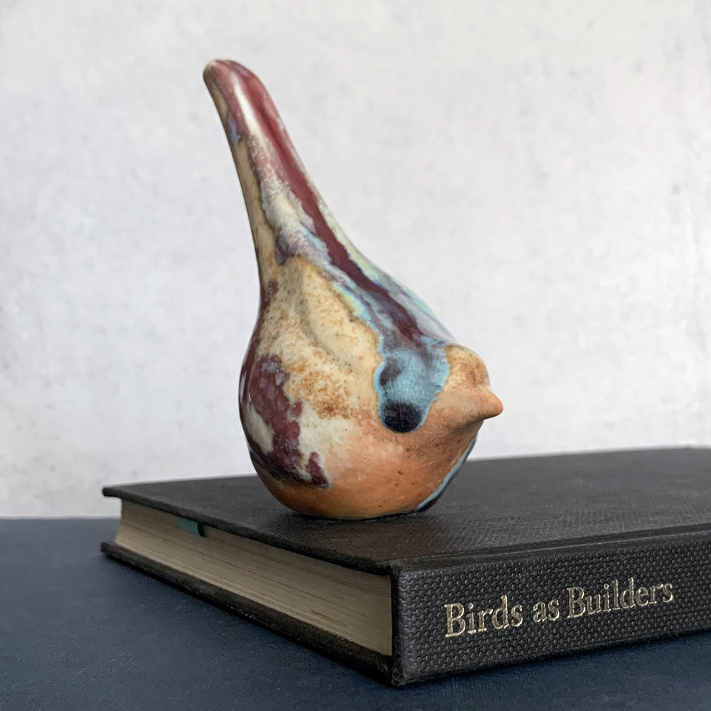 Small ceramic sculpture of a bird, glazed in a rust, cream and blue glaze by artist Becky Story. 