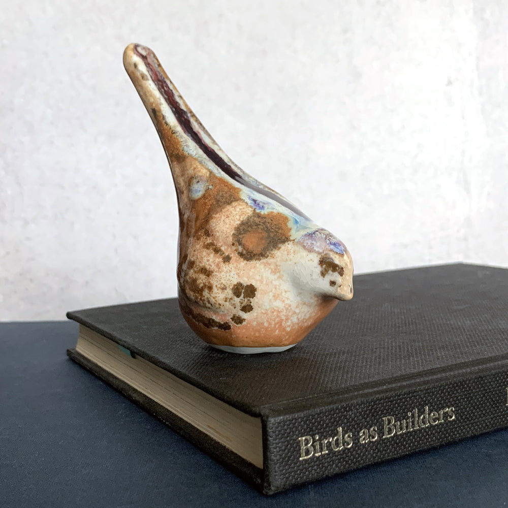 Small ceramic sculpture of a bird, glazed in a rust, cream and blue glaze by artist Becky Story. 