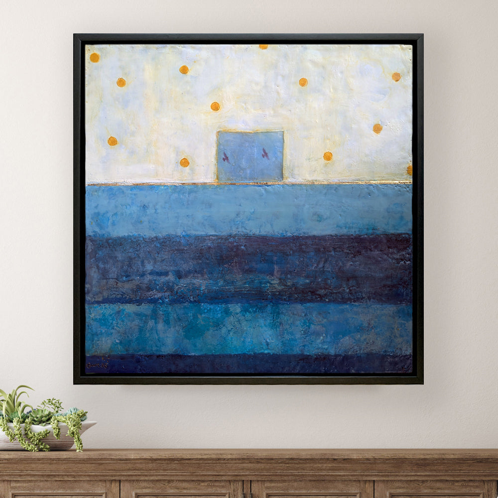 "Let Us Expand Our Vision, and Embrace Our Oneness" painting by Bridgette Guerzon Mills. A mixed media encaustic artwork with two small birds in flight at the center inside a blue box. Blue stripes below and white with yellow dots above.  Shown on a white wall above a table.
