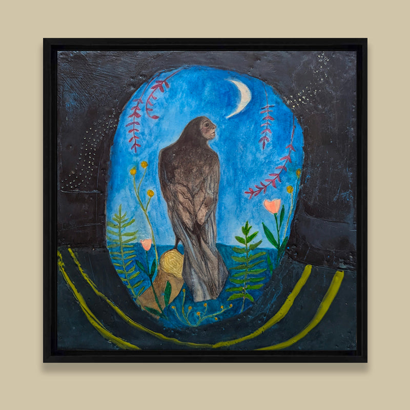 Framed mixed media encaustic painting featuring a mythical creature, a combination of raven and woman, perched on a branch under a night sky and crescent moon. She is surrounded by leaves, and pink and yellow flowers. Displayed on tan wall. 