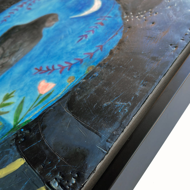 Framed mixed media encaustic painting featuring a mythical creature, a combination of raven and woman, perched on a branch under a night sky and crescent moon. She is surrounded by leaves, and pink and yellow flowers. Side frame detail shown.