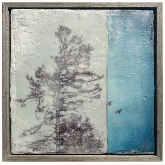 "Surrender" mixed media encaustic painting by Bridgette Guerzon Mills. Framed artwork featuring a textured background, with a tree silhouette on the left and a blue sky with birds on the right.