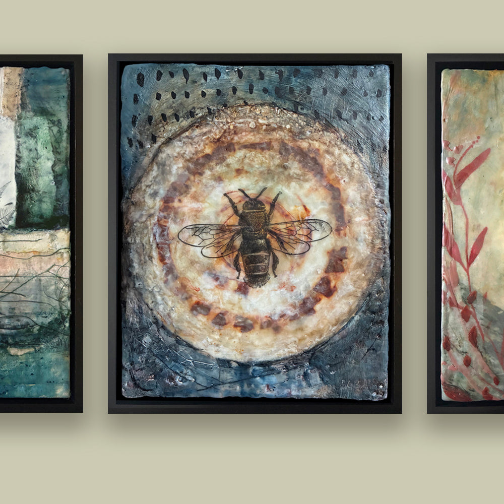 Framed artwork with a bee on a circular design, hung with two other paintings on a beige wall. 