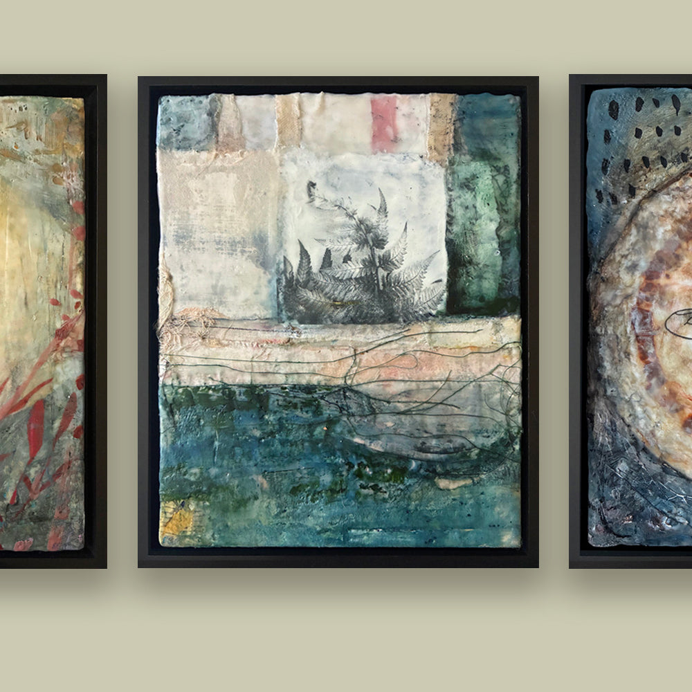 Framed mixed media artwork with a fern detail, hung with two other paintings on a beige wall. 
