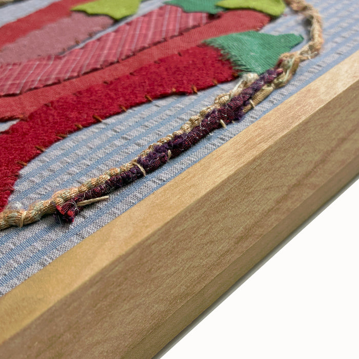 Bunch of Chilies textile collage by artist Hannah Goff. The artwork is comprised of hand-sewn, reclaimed and recycled fabrics, and features five red chilies. Finished in a handmade rustic wood frame, detail view shown.