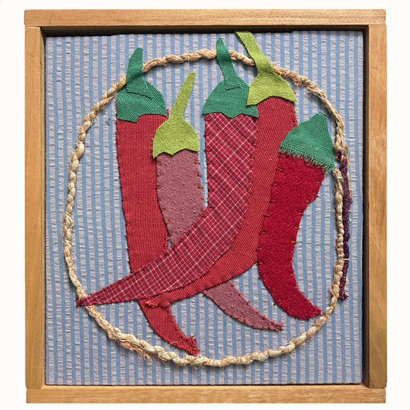 Bunch of Chilies textile collage by artist Hannah Goff. The artwork is comprised of hand-sewn, reclaimed and recycled fabrics, and features five red chilies. Finished in a handmade rustic wood frame.