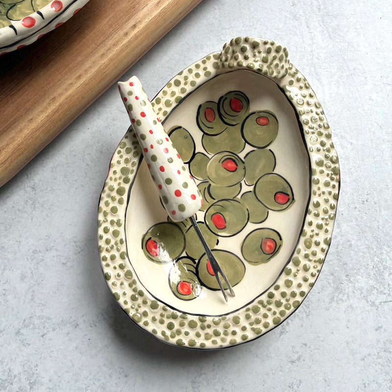 Handmade ceramic olive dish and fork by Molly Lithgo. Textural dish with green olive decoration. Fork with red and green spotted handle. Top view.  