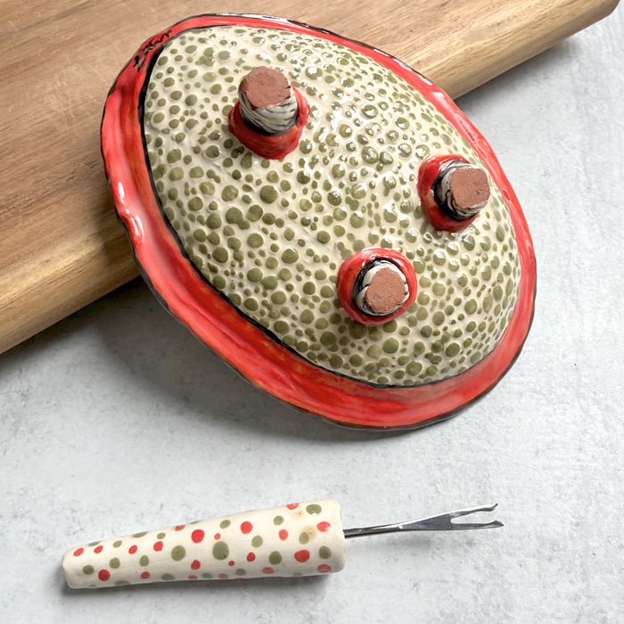 Handmade ceramic olive dish and fork by Molly Lithgo. Textural dish with green olive decoration. Fork with red and green spotted handle. Bottom view. 