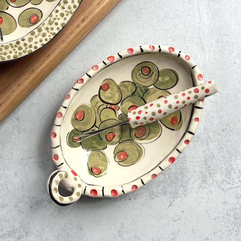 Handmade ceramic olive dish and fork by Molly Lithgo. Oval dish with green olive decoration and polka dots. Fork with red and green spotted handle. Top view.  