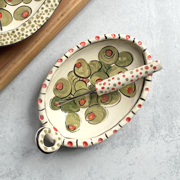 Handmade ceramic olive dish and fork by Molly Lithgo. Oval dish with green olive decoration and polka dots. Fork with red and green spotted handle. Top view.  