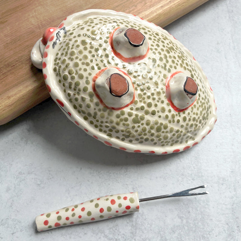 Handmade ceramic olive dish and fork by Molly Lithgo. Oval dish with green olive decoration and polka dots. Fork with red and green spotted handle. Bottom view. 