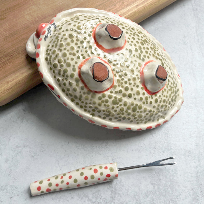 Handmade ceramic olive dish and fork by Molly Lithgo. Oval dish with green olive decoration and polka dots. Fork with red and green spotted handle. Bottom view. 
