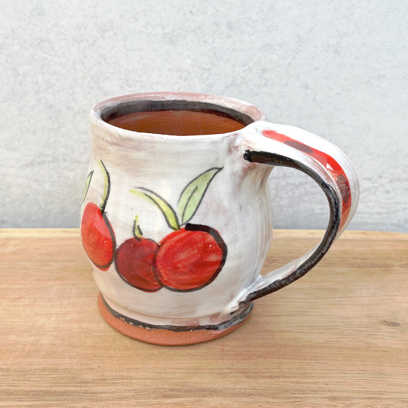 Handmade ceramic mug by NC potter Molly Lithgo. White with cherry decoration. View with handle detail.