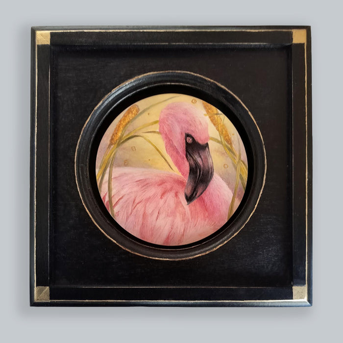A 6" circular painting of a pink flamingo among yellow-green reeds set in a square black frame with gold leaf details.  Artwork by Diane Savino, displayed on pale grey wall. 
