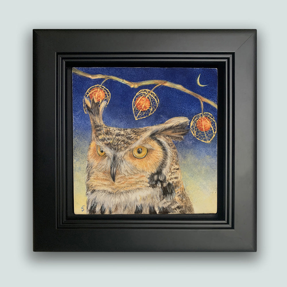 "Night's Awakening" painting by Diane Savino. A great horned owl sits under a brilliant blue night sky with crescent moon. A branch with three Chinese lantern flowers hangs overhead. The egg tempera and gold leaf painting is set in a black frame. Shown on pale blue wall.