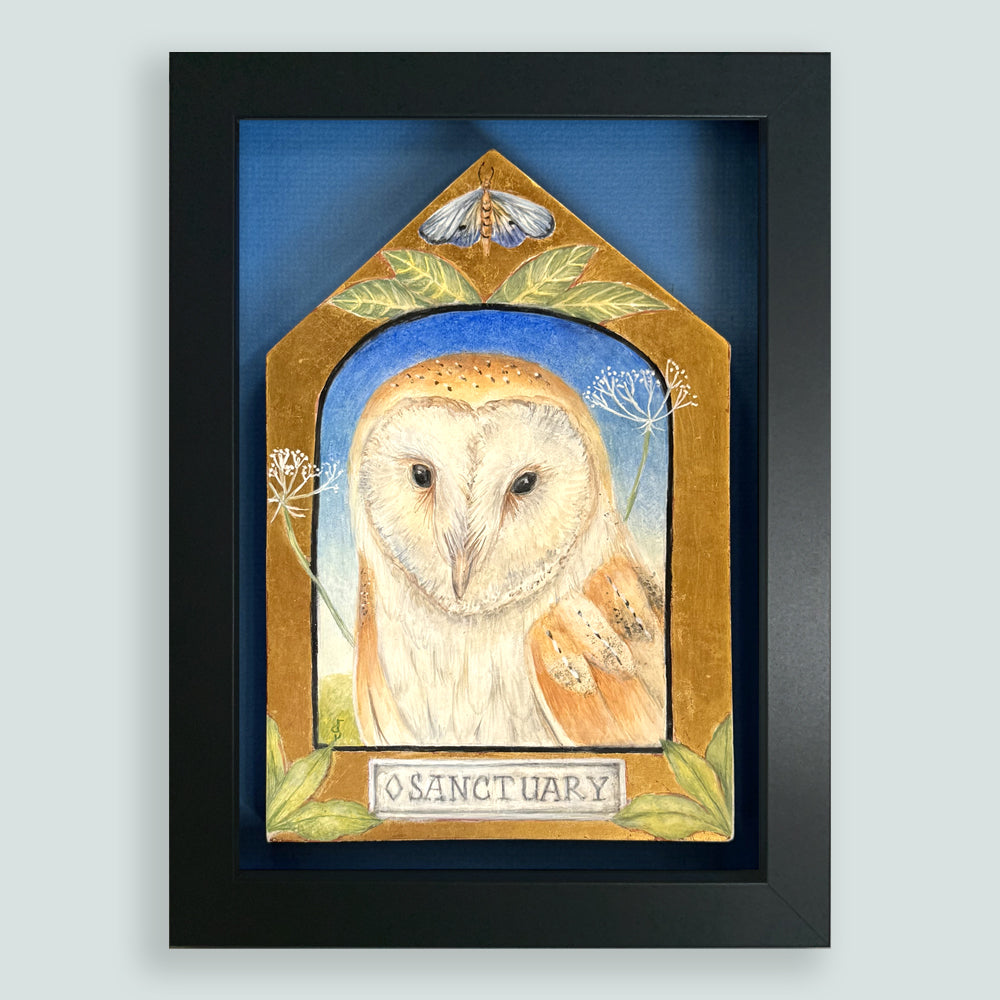 Sanctuary painting by Diane Savino, an owl sits inside a vignette on a house shaped form with foliage and a moth on top. Framed in black and shown on a light blue wall.
