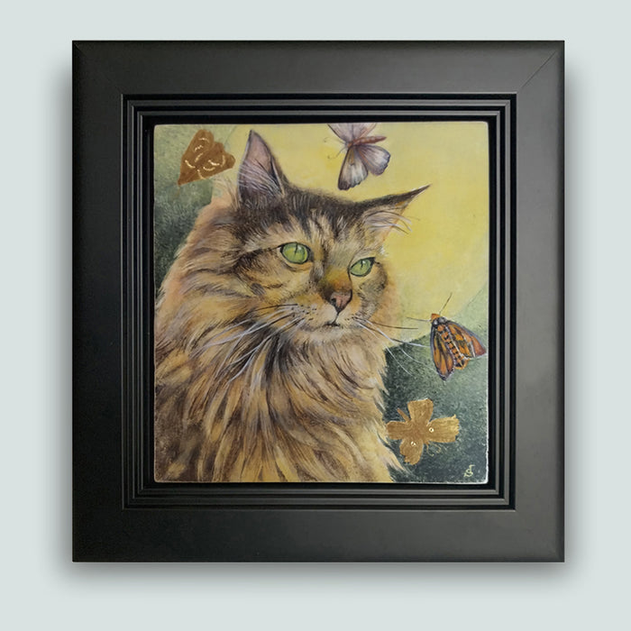 Under the Hunter Moon painting by Diane Savino, a cat sits under a golden moon and is surrounded by moths. Framed in black and shown on a light blue wall.