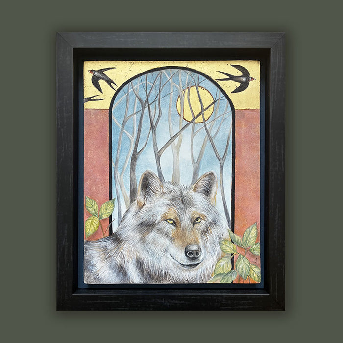 Illustrative egg tempera and gold leaf painting featuring a gray wolf in the foreground, an arched window-like scene with bare trees and a golden moon, two birds at the top, and red-orange side panels. The artwork, by Diane Savino, is set in a dark brown frame and displayed on dark green wall.