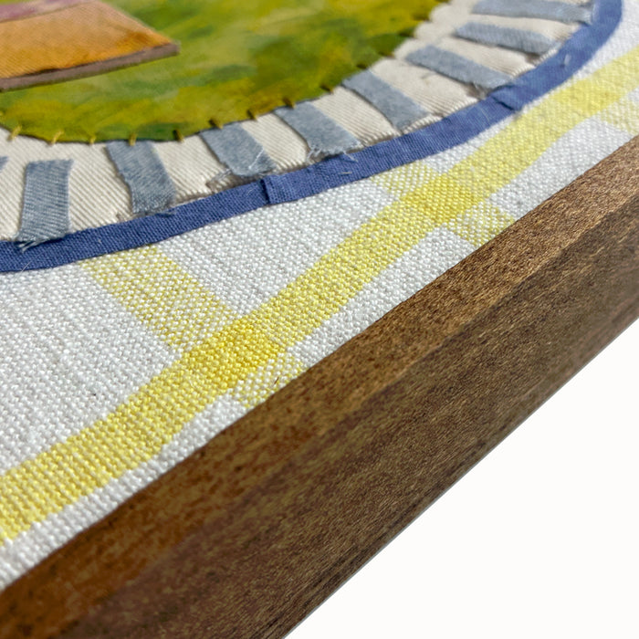 Fruit Bowl textile collage by artist Hannah Goff. The artwork is comprised of hand-sewn and painted, reclaimed and recycled fabrics. It features a pear, cantaloupe slice, a peach, and an apple in a bowl, with three blueberries to the side. Finished in a handmade rustic wood frame, side detail shown.